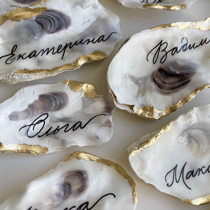 Natural oyster shell wedding place cards with black calligraphy and gold leaf edges.