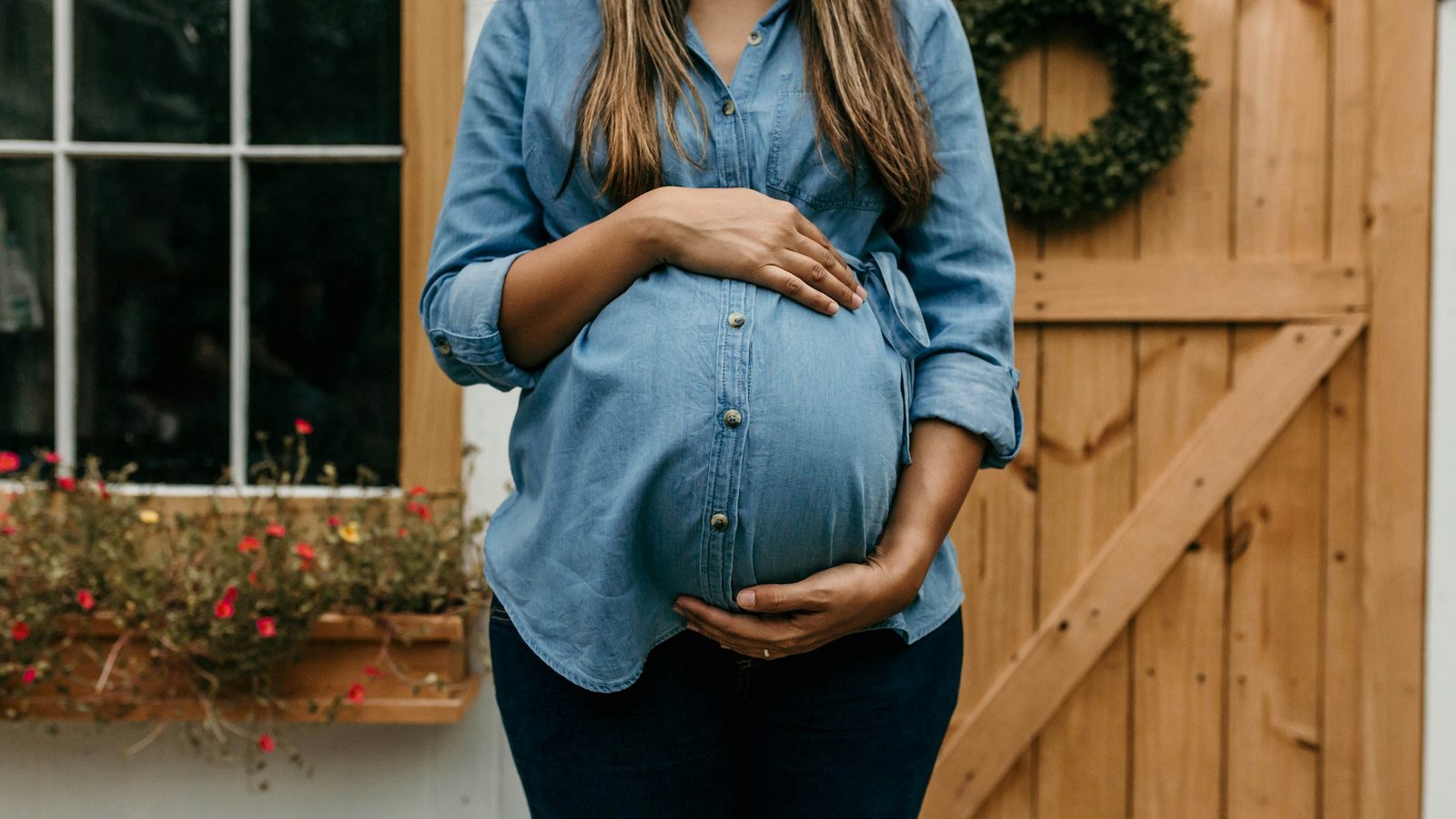 Pregnant self-employed woman standing in front of a wooden workshop door