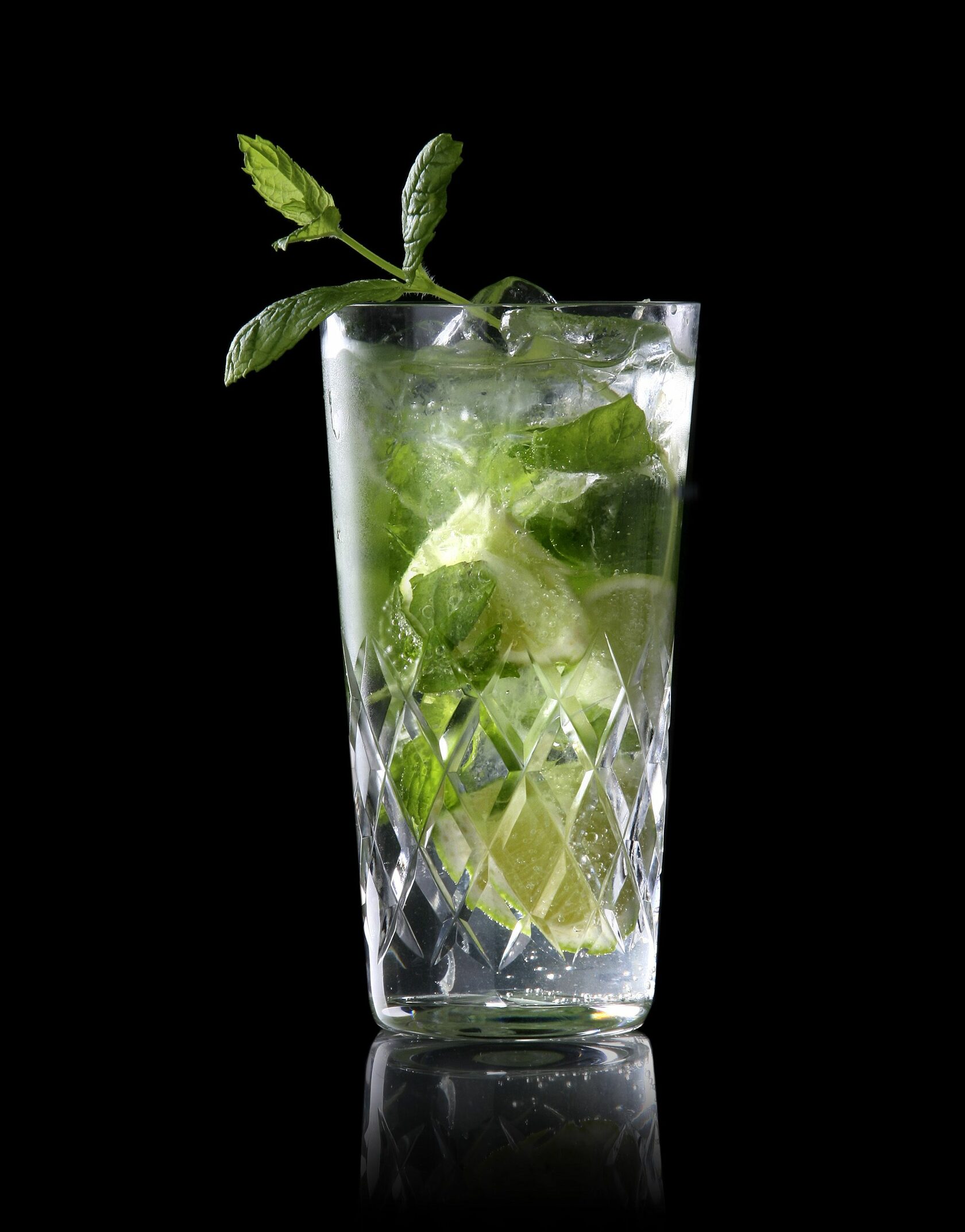 коктейль мохито в стакане хайбол на черном фоне с украшением мятой и лаймом, также видны листья мяты внутри стакана