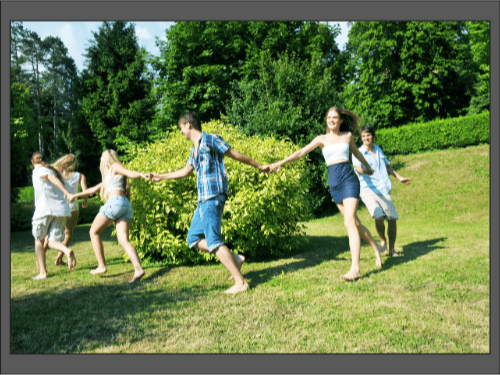 Группа молодых людей играет на траве, держась за руки и бегая вокруг куста.