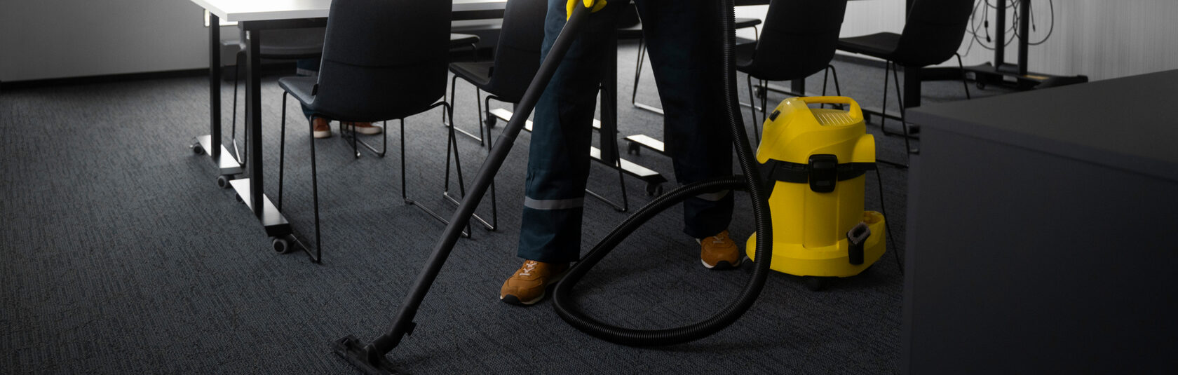 Клинер пылесосит ковровое покрытие в офисном помещении.