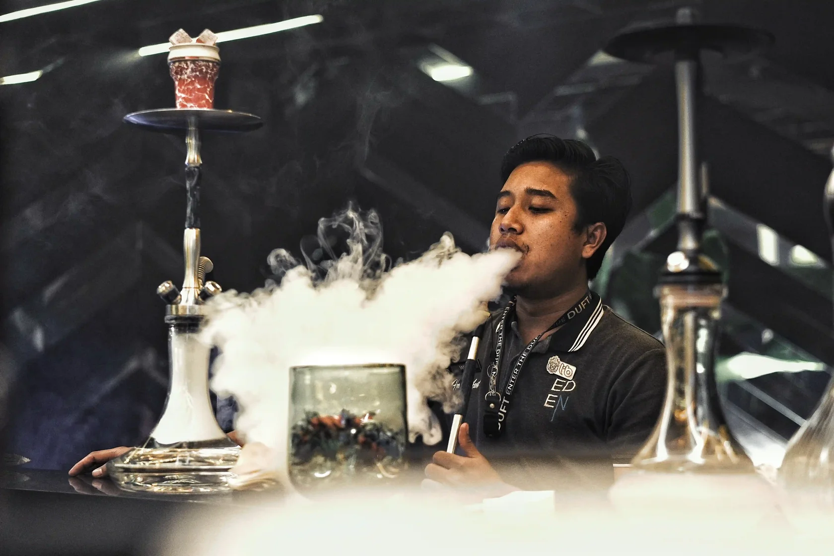 An expert hookah master at Eden Hookah Club demonstrating how to get thicker shisha smoke clouds by exhaling a massive, dense cloud over the bar.