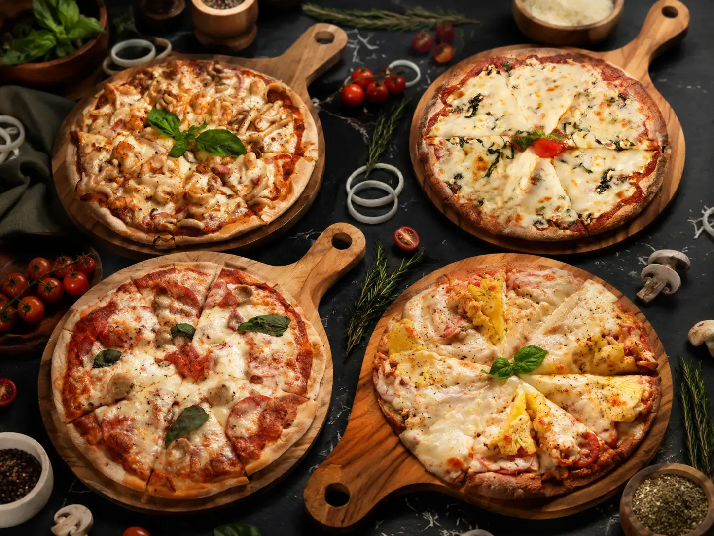 Four pizzas from Eden Uluwatu served on wooden boards with fresh herbs and ingredients