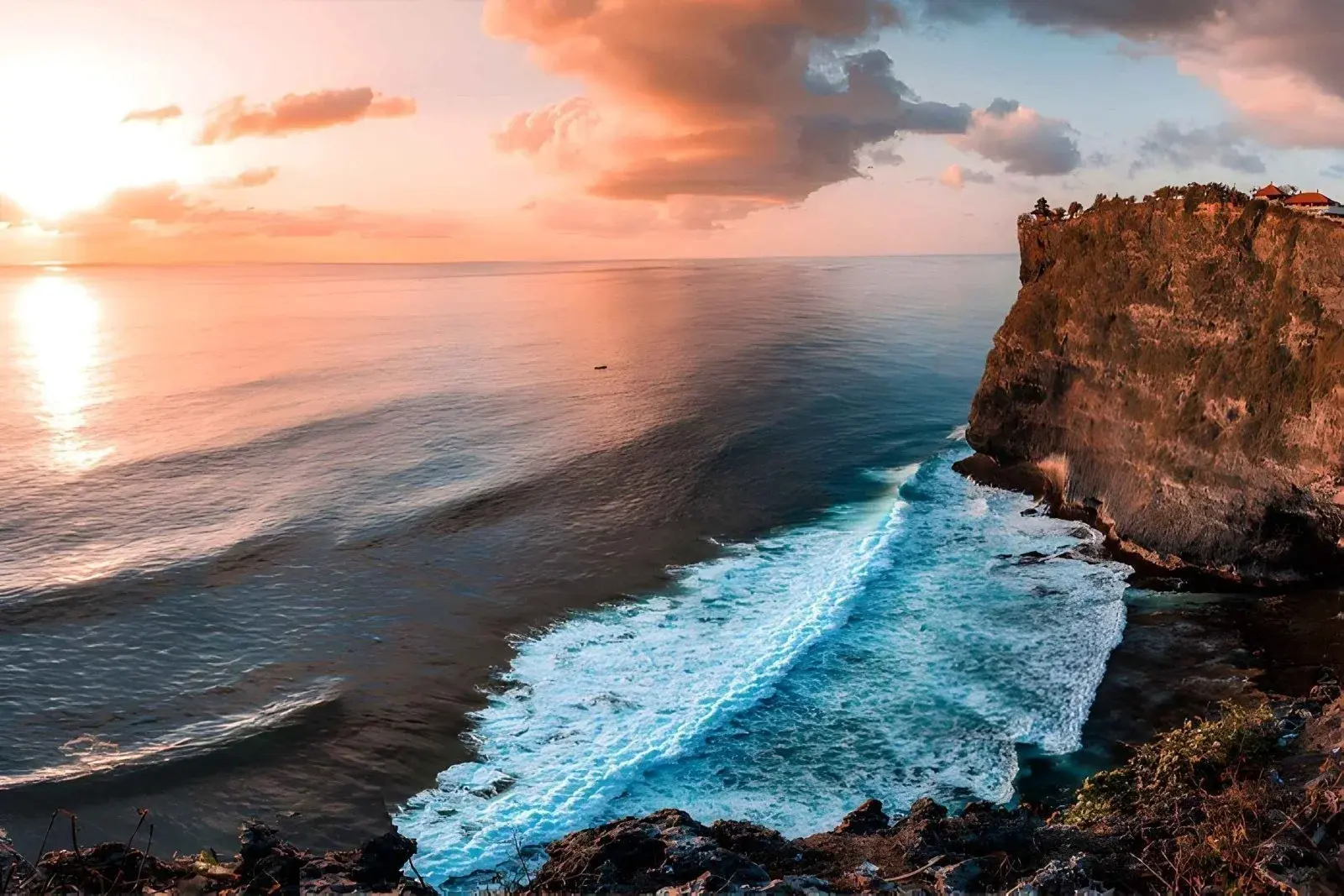 A breathtaking view of the ocean crashing against a dramatic cliffside in Uluwatu during a pink sunset, an ideal way to start exploring what happens in Bali on Wednesday.