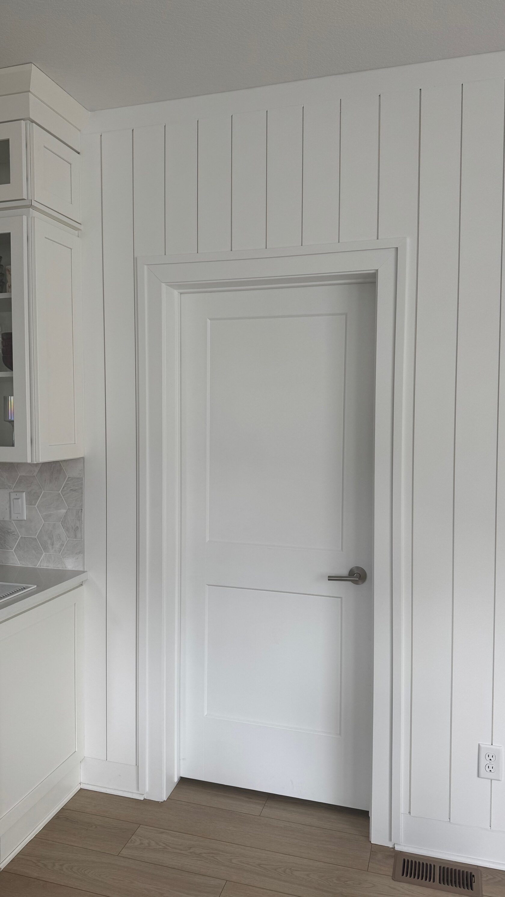 White shiplap paneling fitted around a doorway with coordinating white trim.