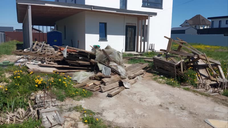 Груда старых досок и строительного мусора на участке у недостроенного дома