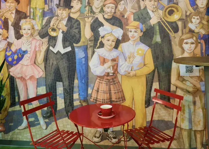 A red table with a cup of coffee by a mosaic mural in the Volga hotel coffee shop
