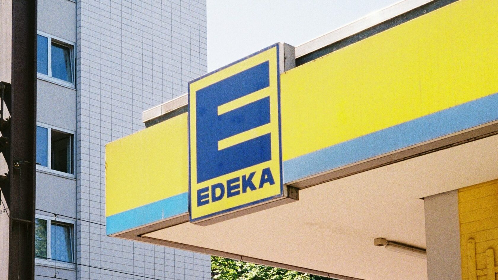 An EDEKA sign on a yellow canopy next to a tall apartment block