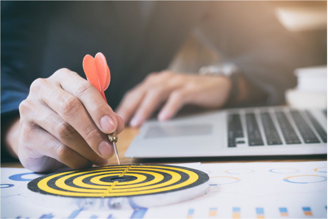 Develop trading strategies: Man with a laptop in one hand and with the other hand he sticks a dart in the center of a board 