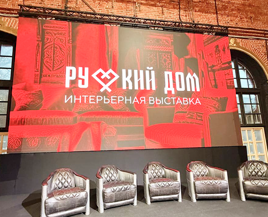Сцена интерьерной выставки «Русский дом» с красным баннером и креслами для спикеров