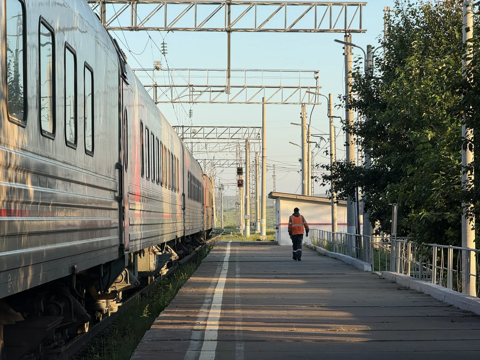 Поезд на станции по дороге в Забайкальск и работник железной дороги в оранжевой жилетке