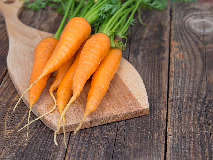 Freshly harvested orange carrots on a wooden cutting board, highlighting the potential for indoor container gardening.