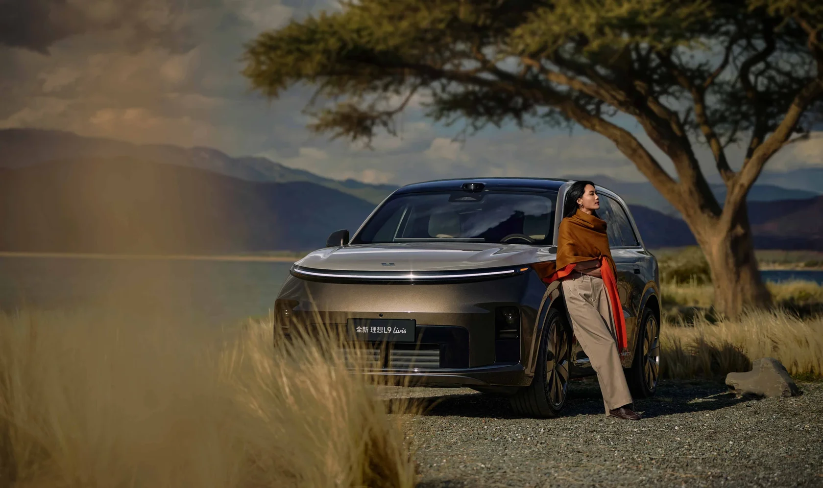 Li Auto L9 на фоне гор и озера, рядом стоит женщина
