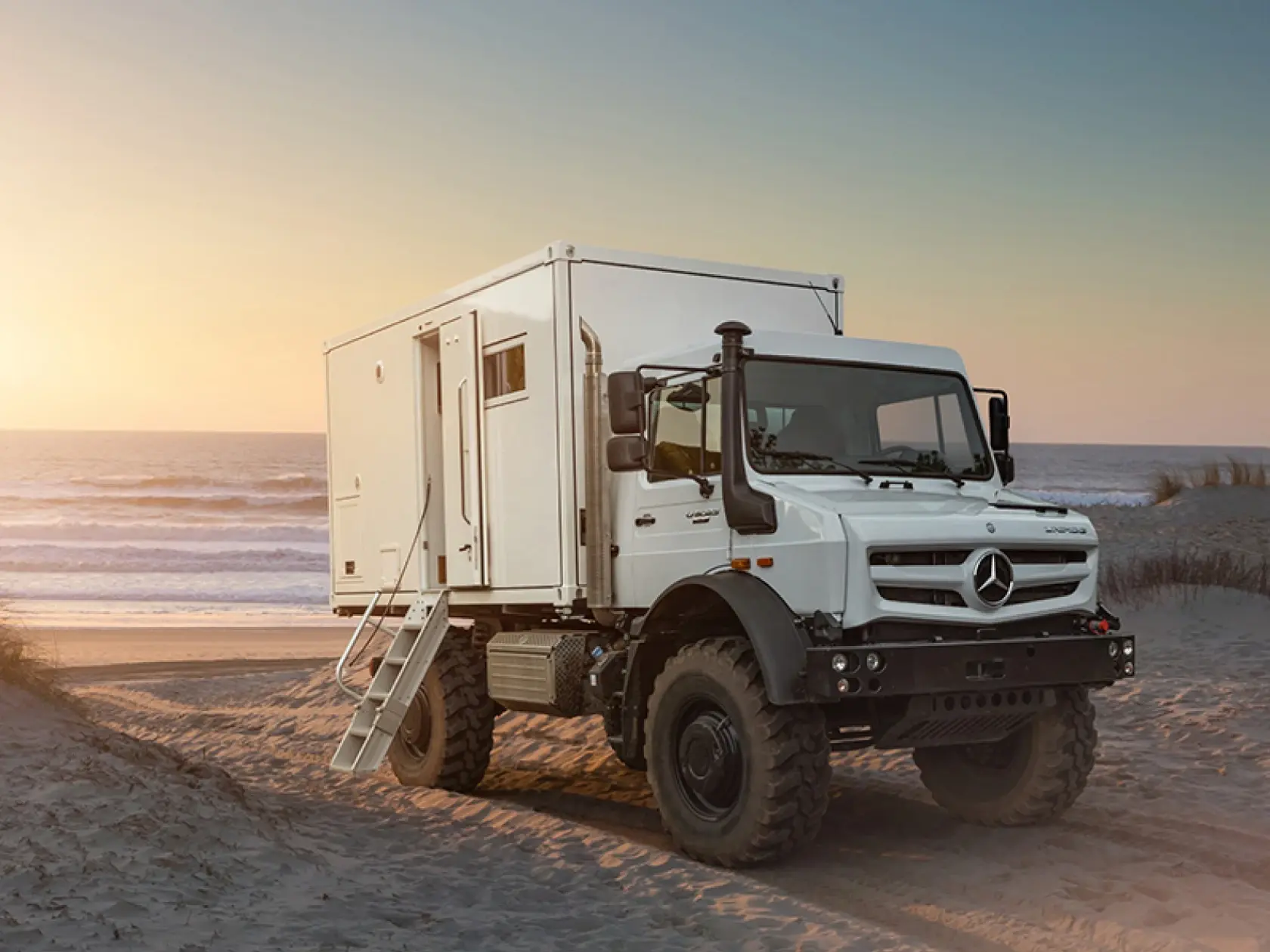Белый Unimog с жилой надстройкой на пляже