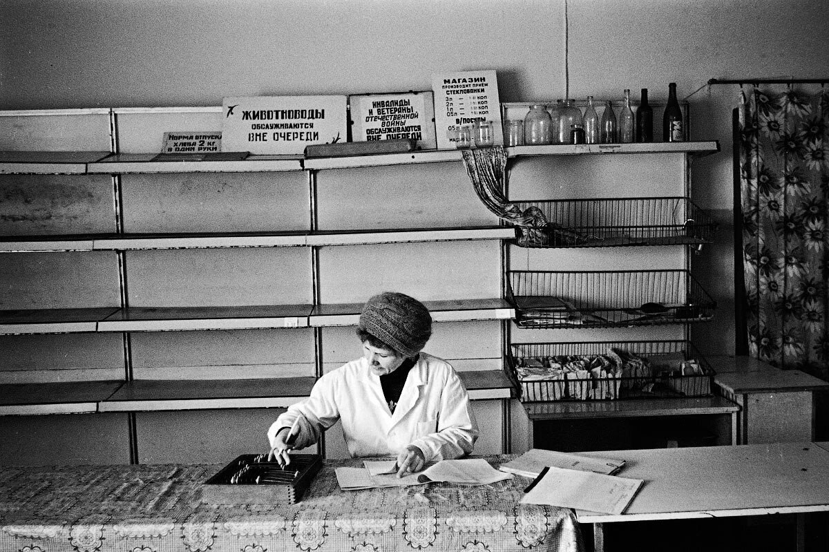 Продавщица в советском магазине, сзади пустые полки, дефицит товаров