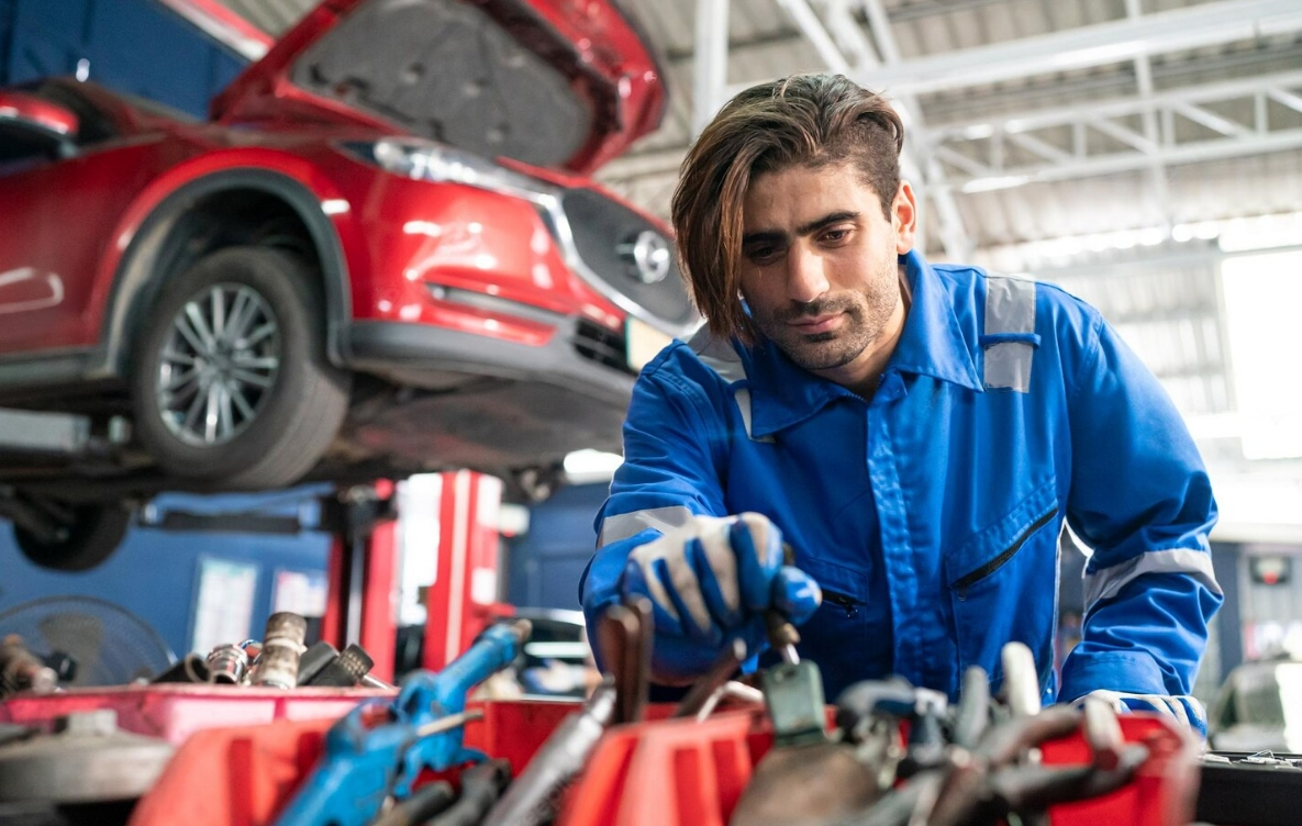 A male car Mechanic is lying on his back and repairing a car.