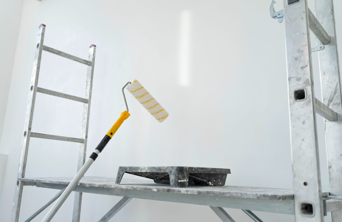 A white wall, next to it a staircase, and on it a basin and a paint roller for painting