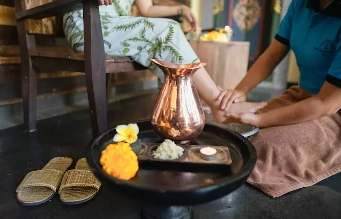 A therapist performing a traditional Balinese foot washing ritual using a copper pitcher, sea salt, and flowers, setting a relaxing tone at a highly recommended best spa in Ubud.