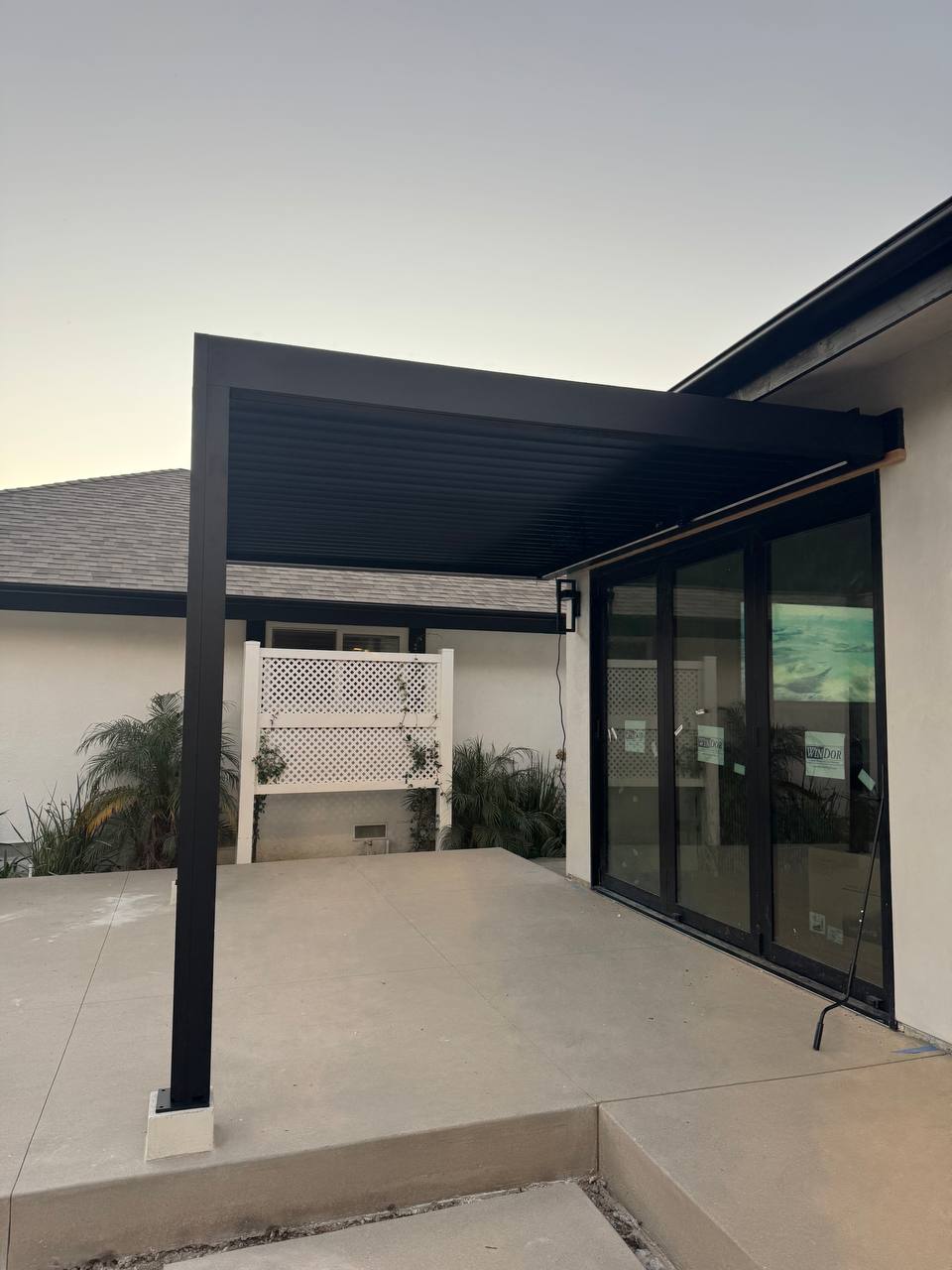 Side view of the black pergola roof attached beside the house and glass patio doors.