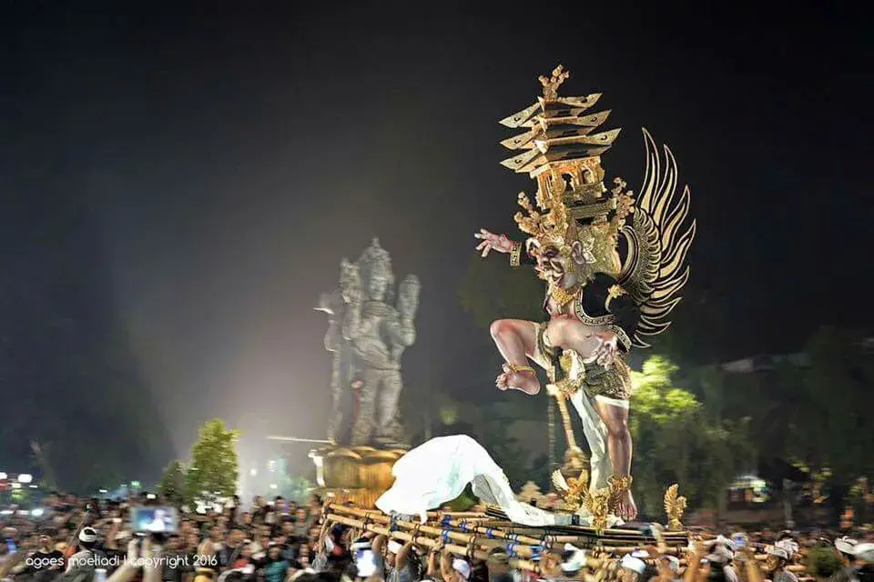 A towering and intricate demon effigy being carried through the streets during the Ogoh Ogoh Bali night parade near the Catur Muka statue, celebrating the Pengerupukan ceremony.