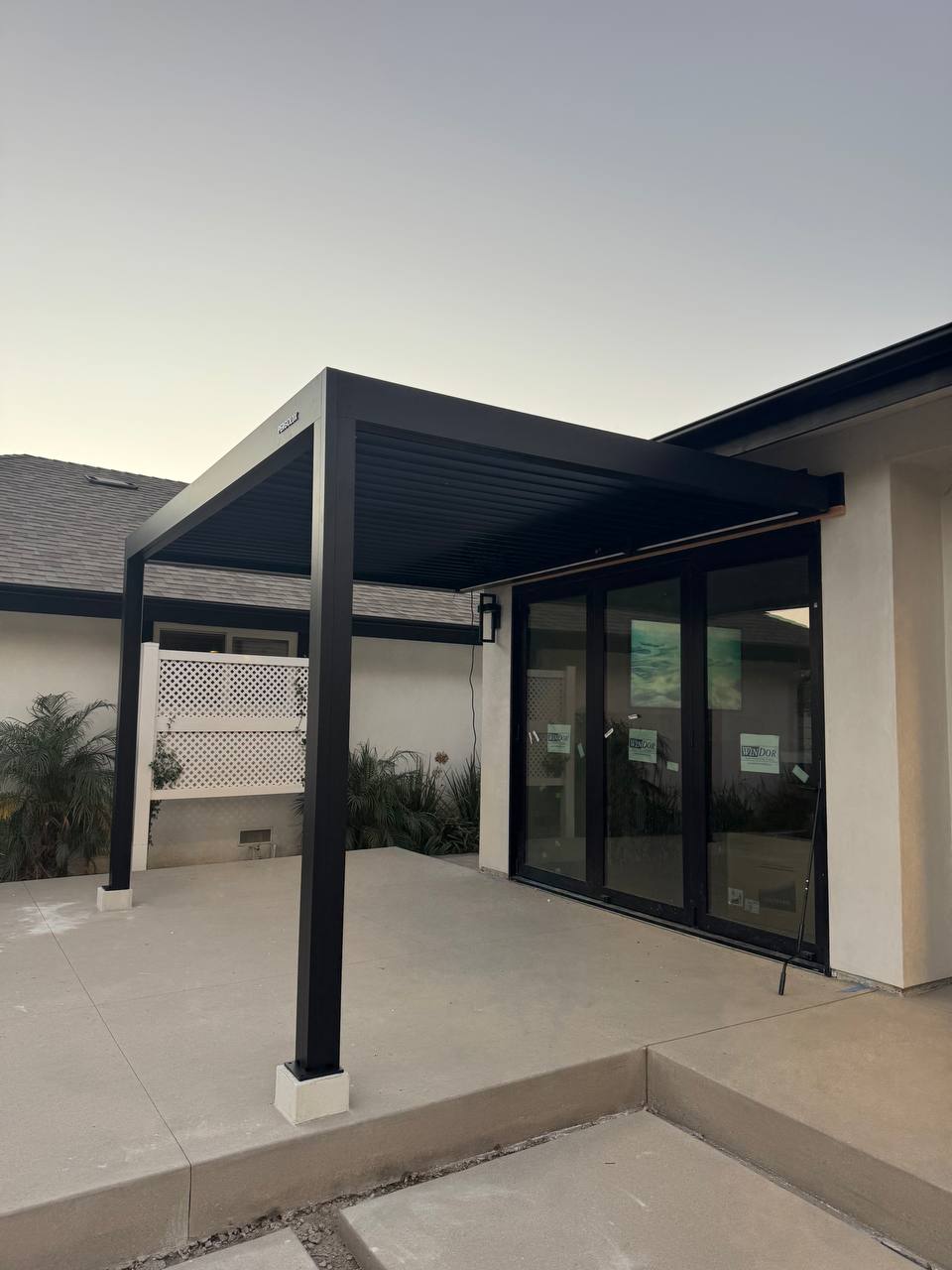 Completed wall-mounted black pergola viewed from the edge of the concrete patio.