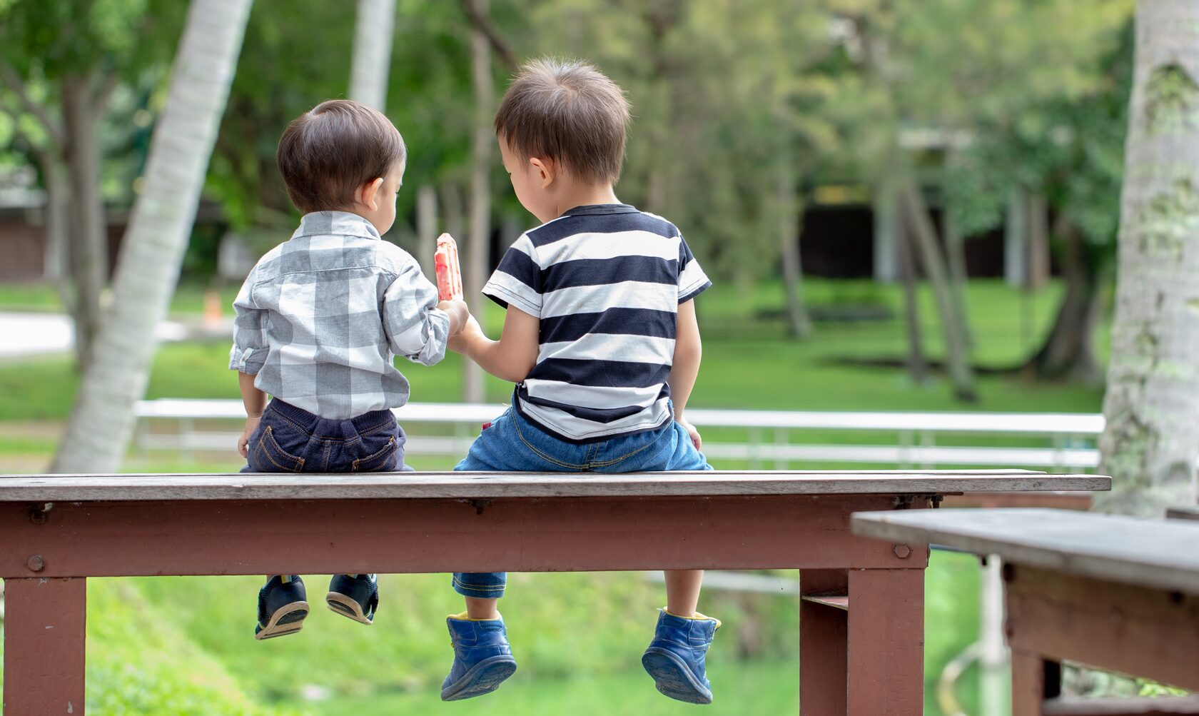 Two boys sat on a bench sharing an icecream