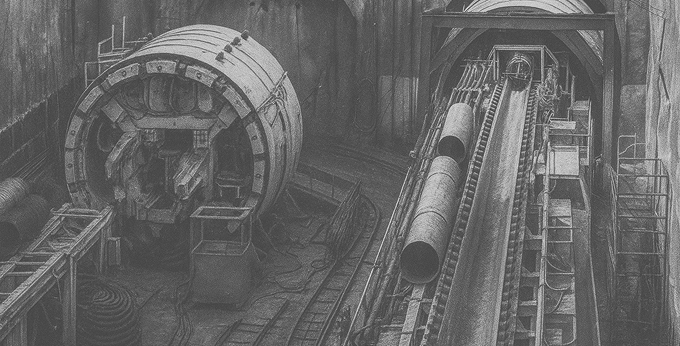 Проходческий щит и оборудование в шахте метро. Рельсы и трубы уходят вглубь тоннеля.