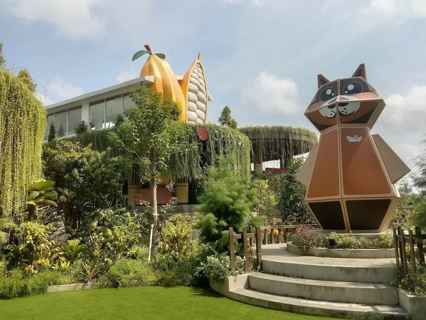 A playful giant civet cat statue and oversized cacao pod architecture surrounded by tropical gardens at Tebasari Coffee & Chocolate in Ubud.