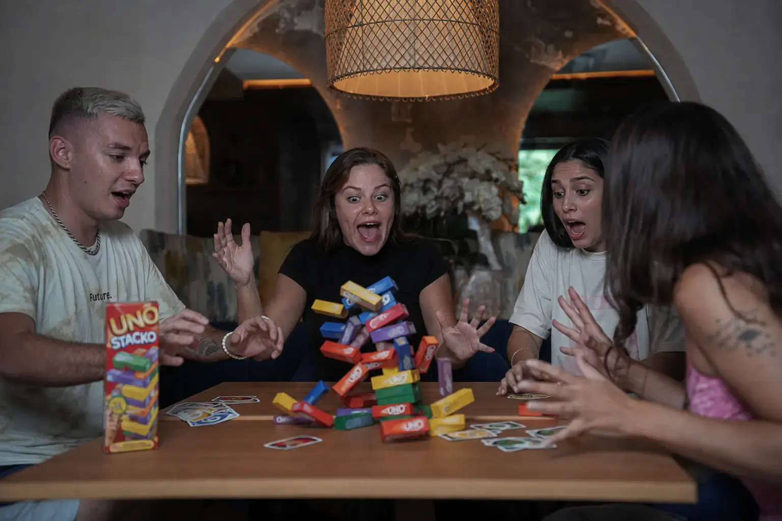 A moment of excitement as a colourful Uno Stacko tower falls during a game among friends at a cozy Shisha Lounge with Table Games in Bali.