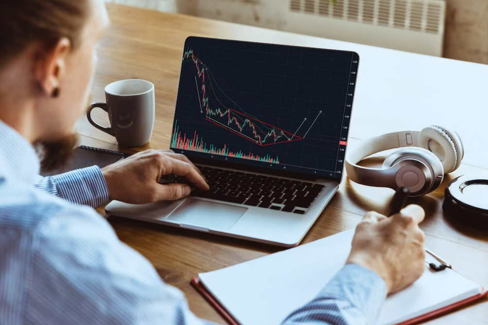  Man writing in a notebook and analyzing price charts on a computer to learn to trade.