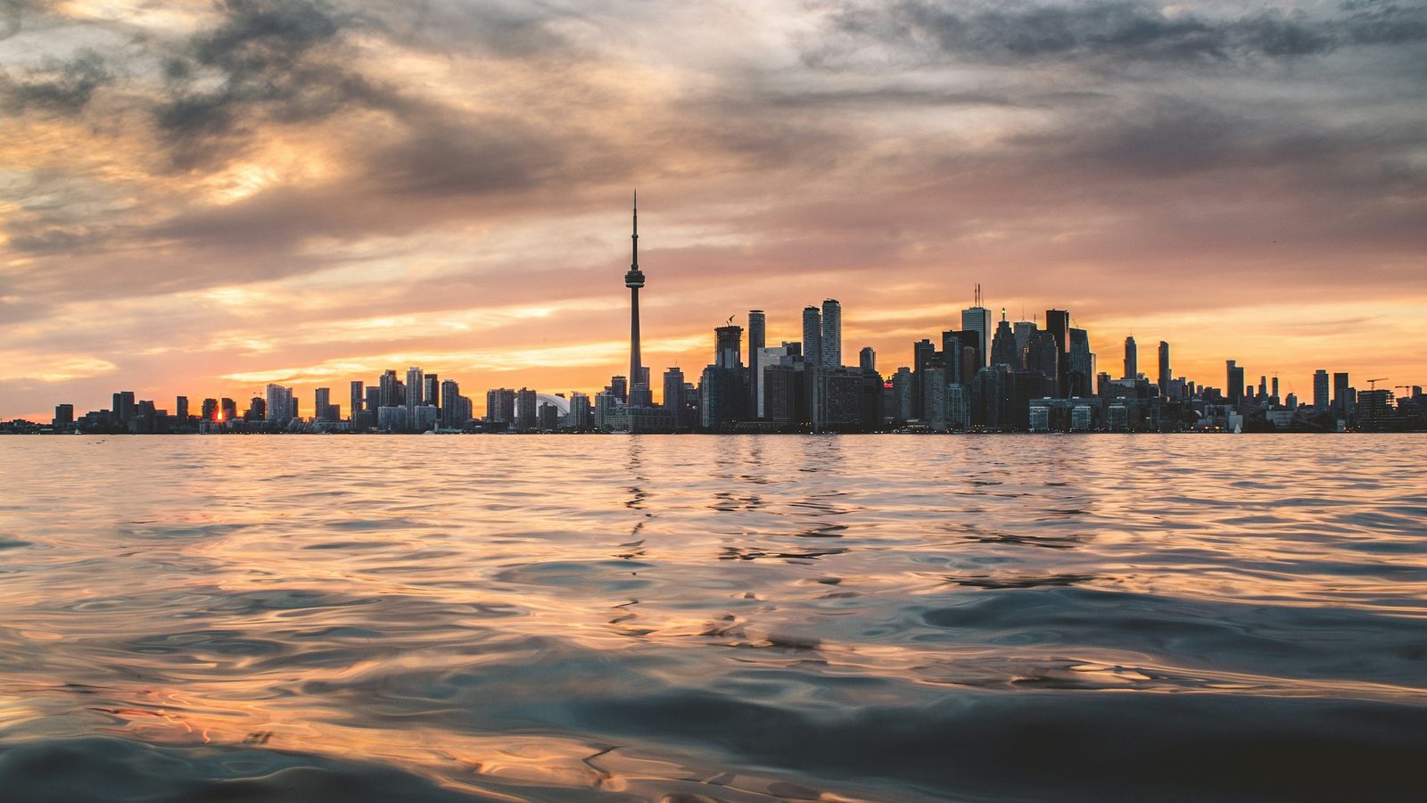 The Toronto skyline with the CN Tower seen across Lake Ontario at sunset, with the water in the foreground
