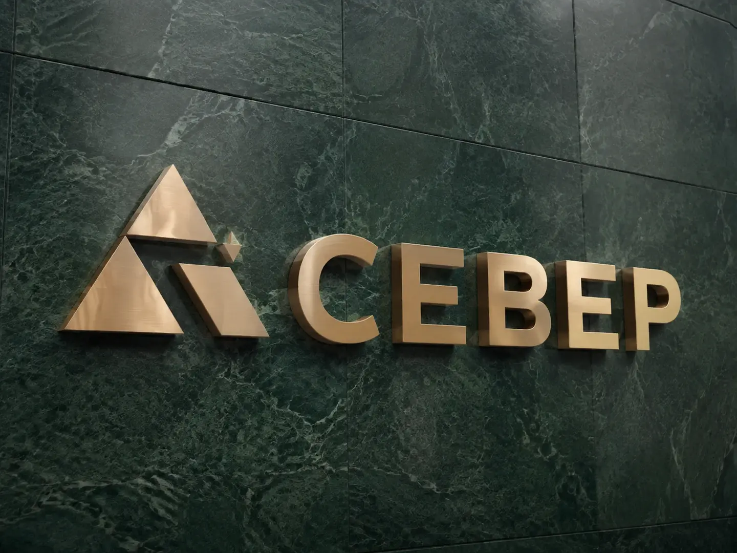 Объёмная латунная вывеска СЕВЕР на зелёной каменной стене с видимыми бортами