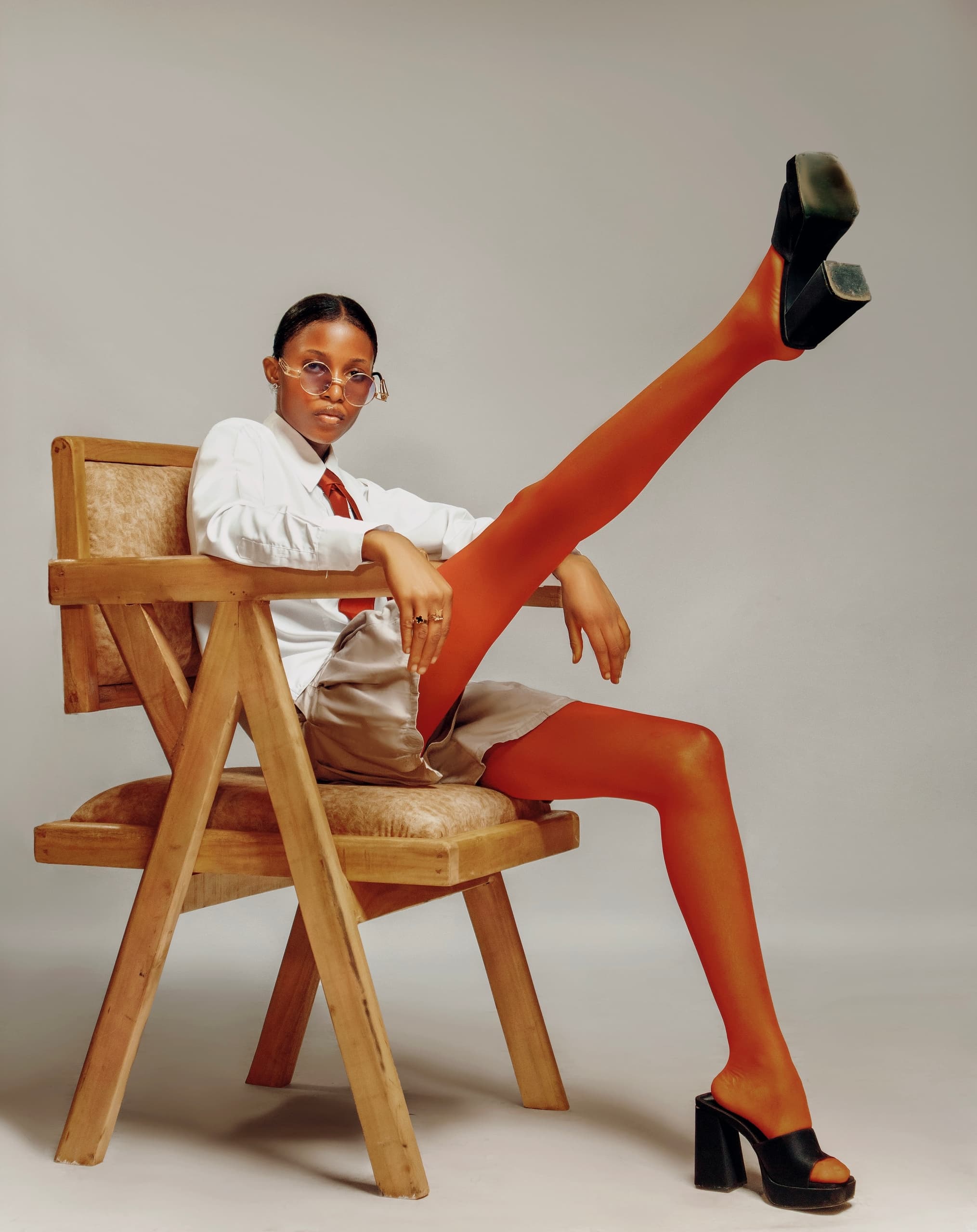 Fashion model in a white shirt and orange tights posing across a wooden chair