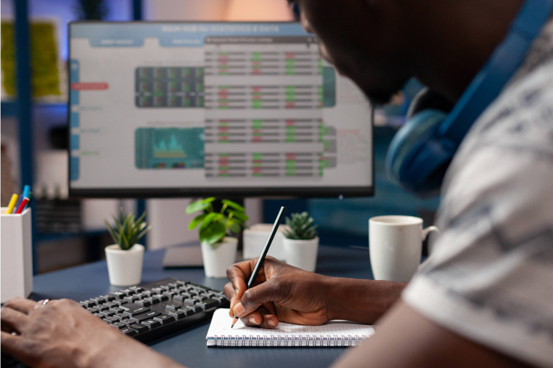 Man writing in his notebook and looking at his computer screen trading images