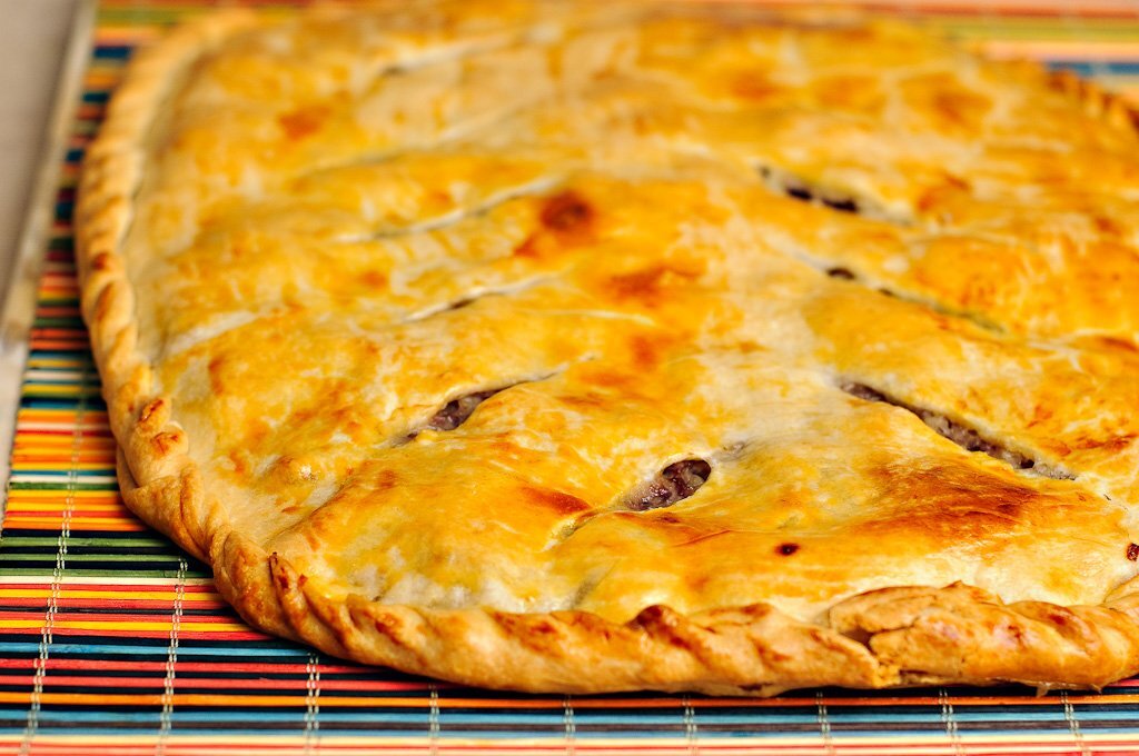 Аппетитная пицца с золотистым коржом, с сочной начинкой из колбасы и свежих помидоров, сыром и зеленью сверху