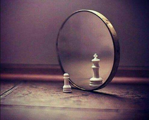 Image: Pawn chess piece in front of mirror that is reflecting the image of a King chess piece.
