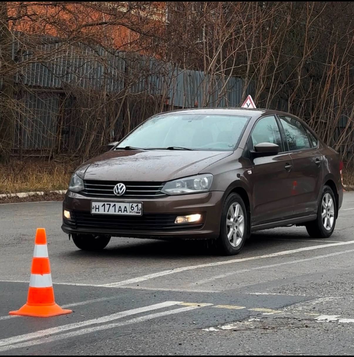 Коричневый учебный Volkswagen Polo на площадке с оранжевым конусом