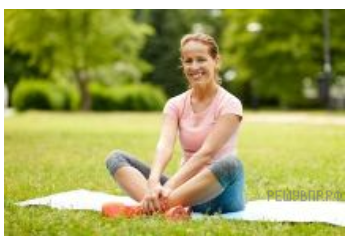 Улыбающаяся женщина сидит на пледе в парке, скрестив ноги