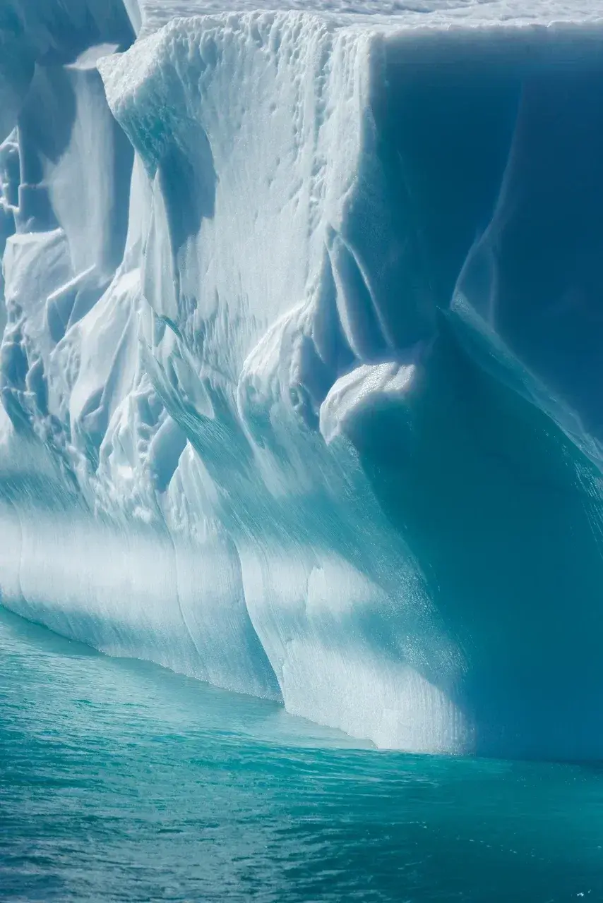 Close-up of a massive blue iceberg rising from turquoise Antarctic waters during an Antarctica expedition.