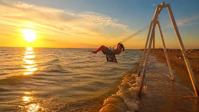 Девушка в парео на качелях у моря на пляже в Должанке