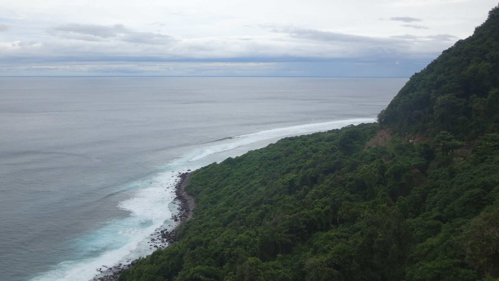 Wide panoramic beach view with rolling waves and dark rocky coastline