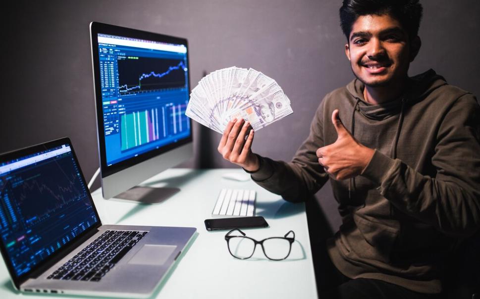How much money do you need to start day trading: A man in front of computers with price charts, holding an initial sum of money to start intraday trading