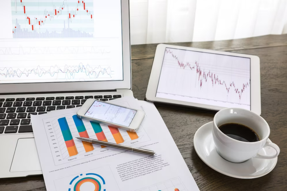 dispositivos tecnológicos con gráficos de trading y taza de café sobre una mesa.