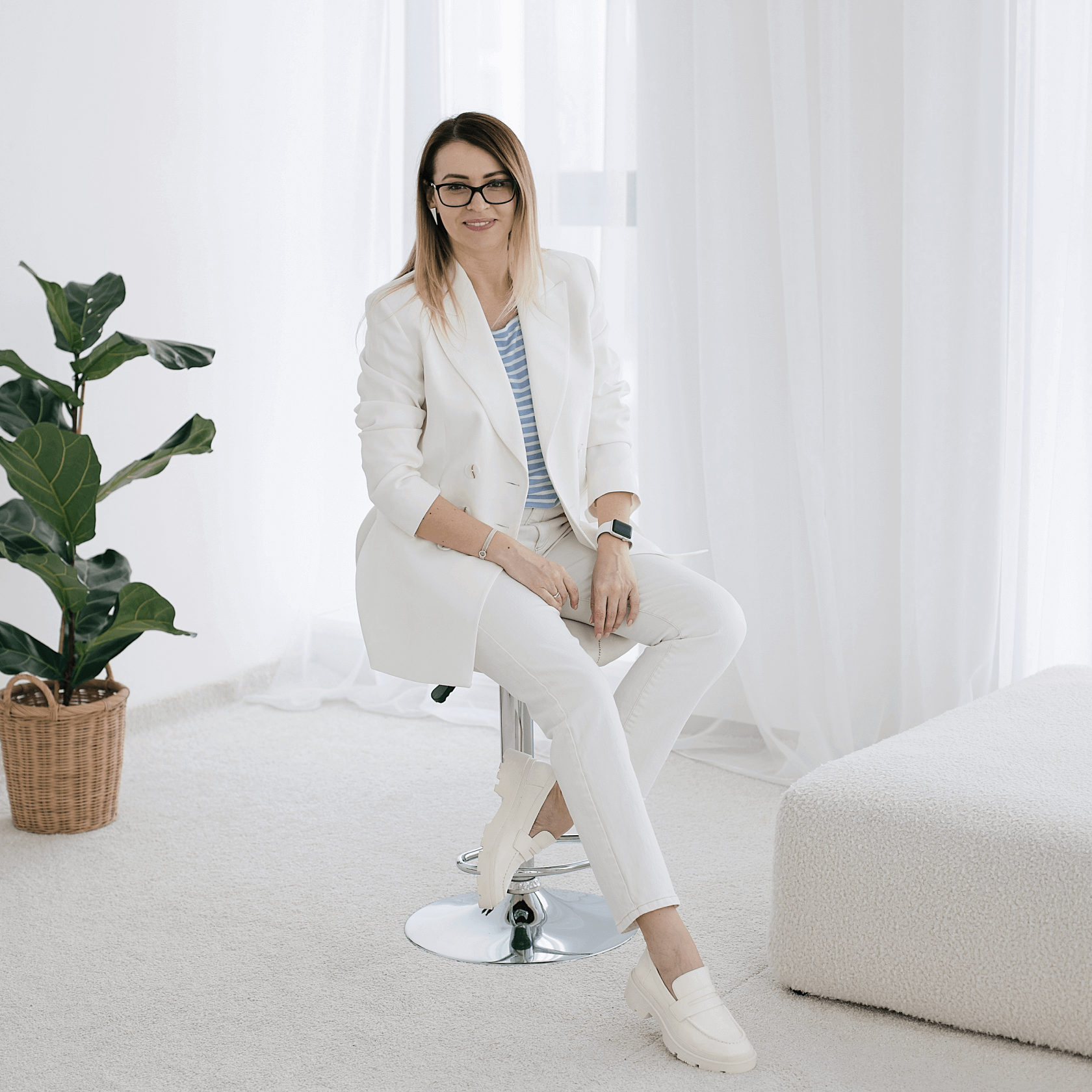 Девушка в белом костюме сидит на стуле и смотрит в кадр