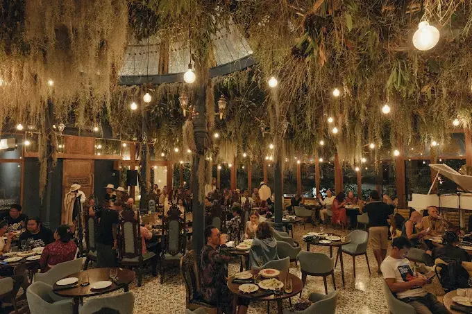 A magical and theatrical top dinner in Ubud, featuring a grand dining room filled with hanging moss, vintage lighting, and an immersive, mystical atmosphere.