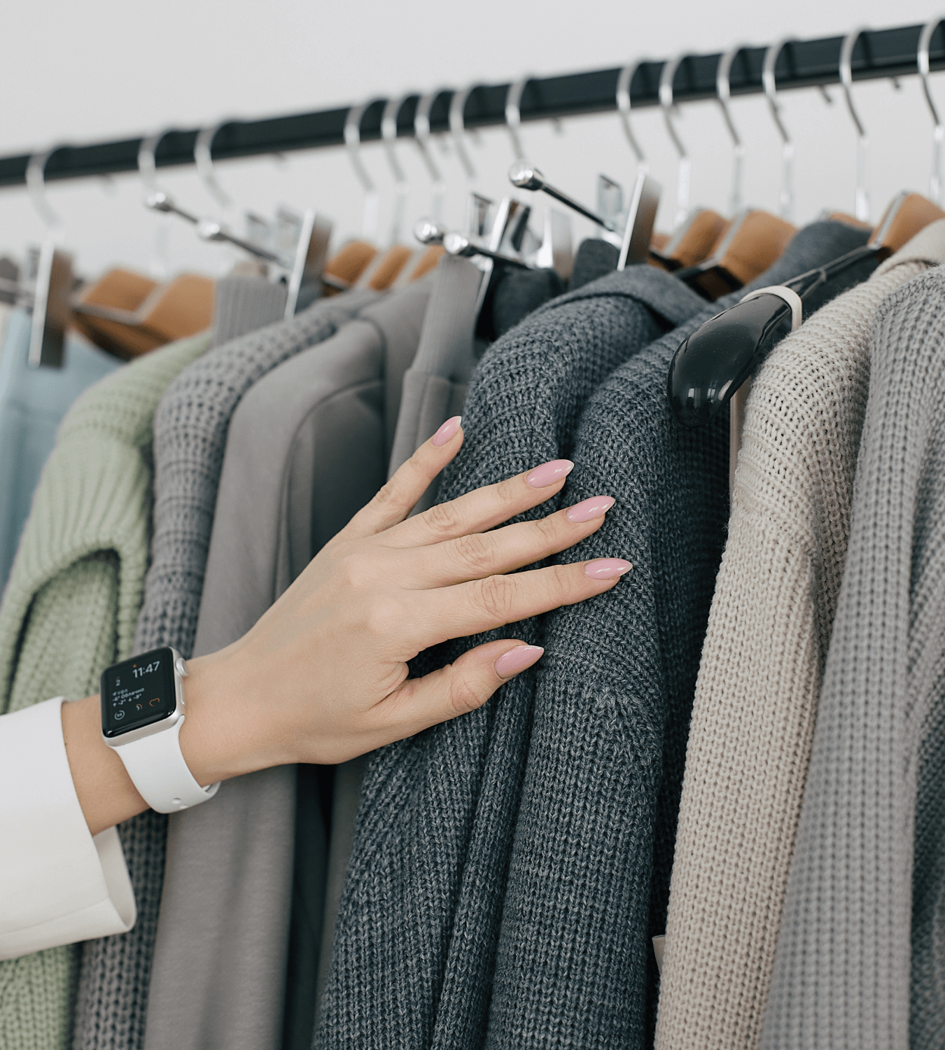 Женская рука трогает вешалки с одеждой