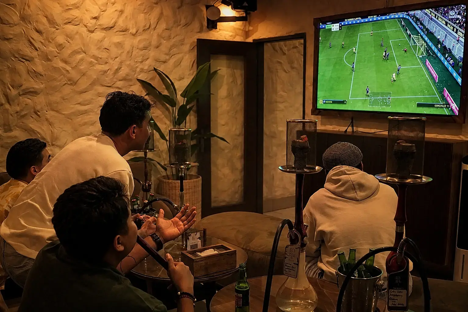A group of friends enjoying console gaming on a large screen in a dedicated VIP room at a Shisha Lounge with Table Games in Bali, with hookah pipes nearby.