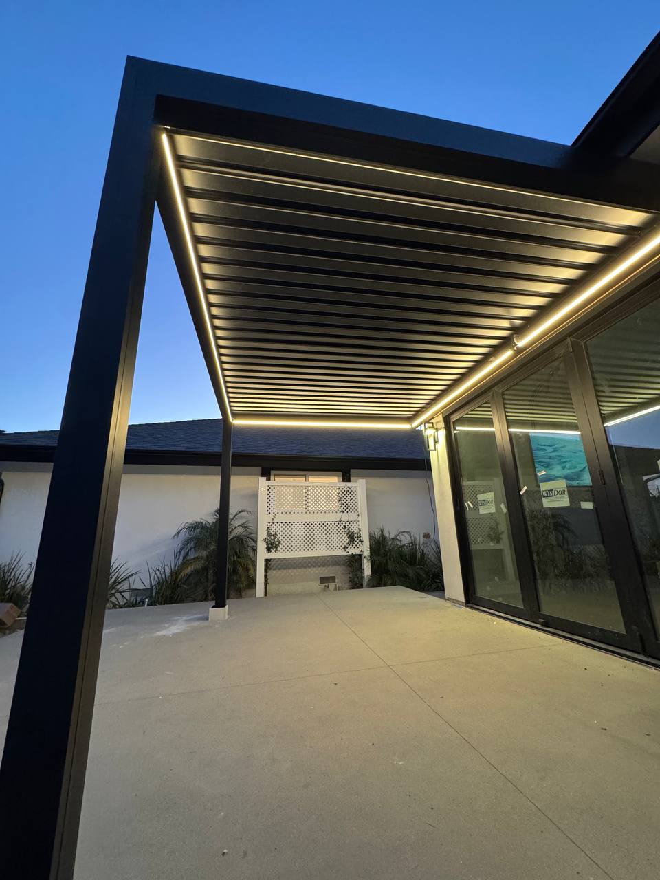 Upward view of the pergola louvers and perimeter LED strips at blue hour.