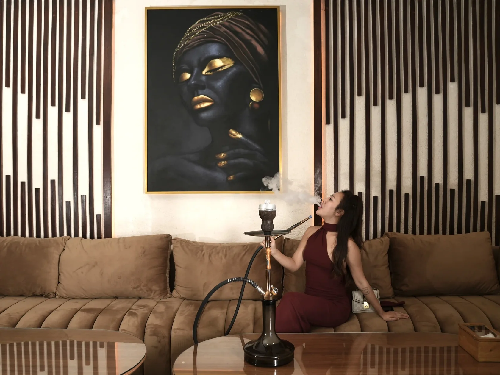 A woman relaxing on a sofa in a beautifully decorated villa room, enjoying a thick cloud of smoke after ordering a premium shisha delivery in Bali.