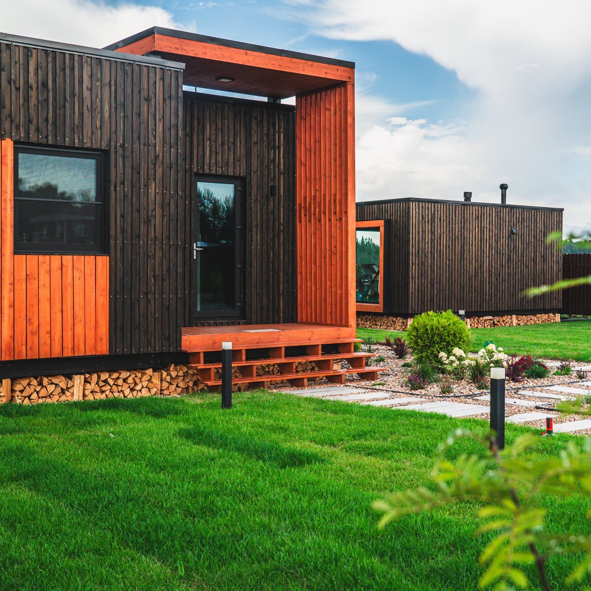 Банно-гостевой дом Country House летом: навес над входом, дровница под террасой, газон
